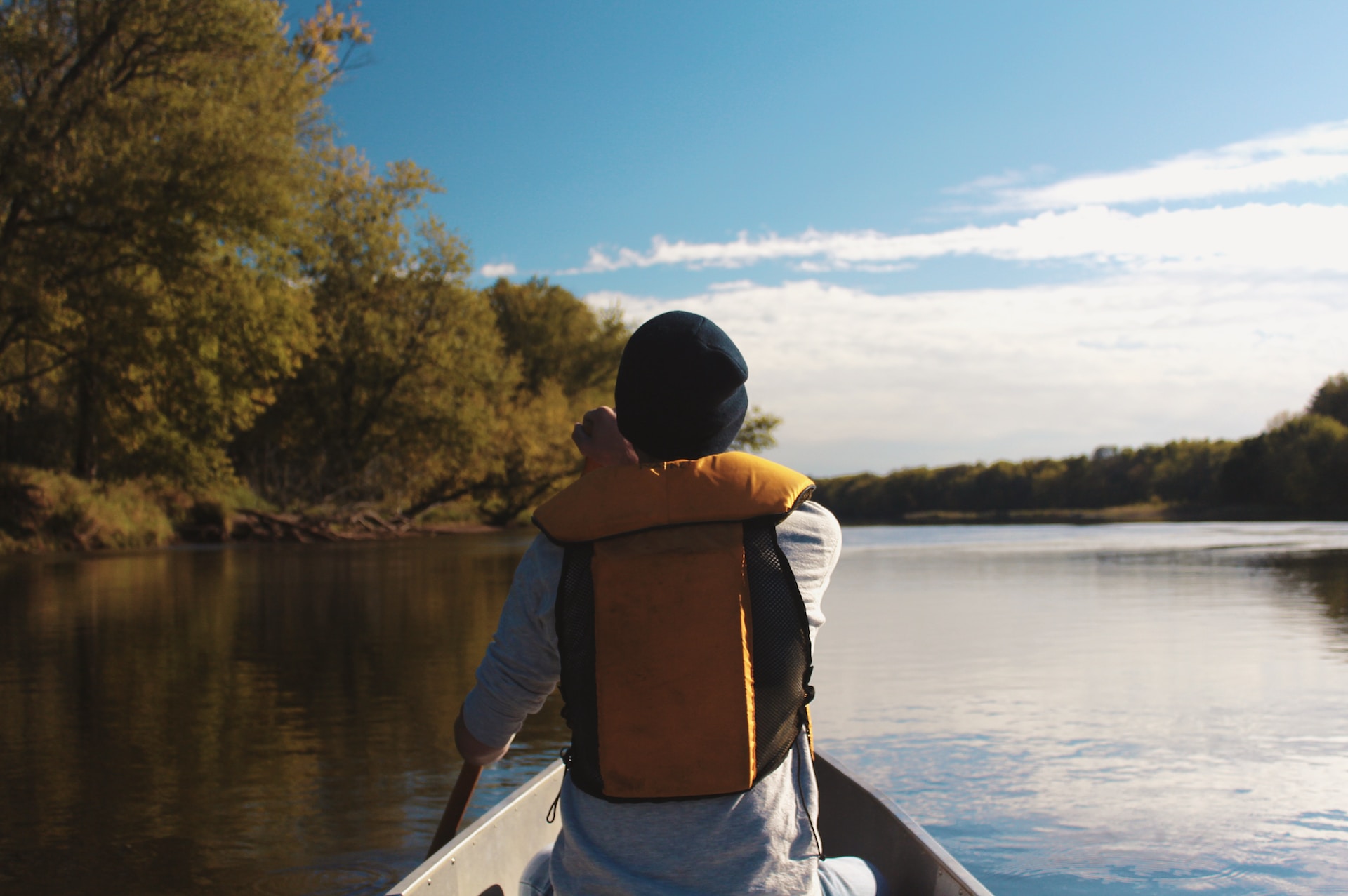 A young man canoeing in a lake looking out onto the horizon. He is wearing a grey sweater, black beanie and yellow life jacket.