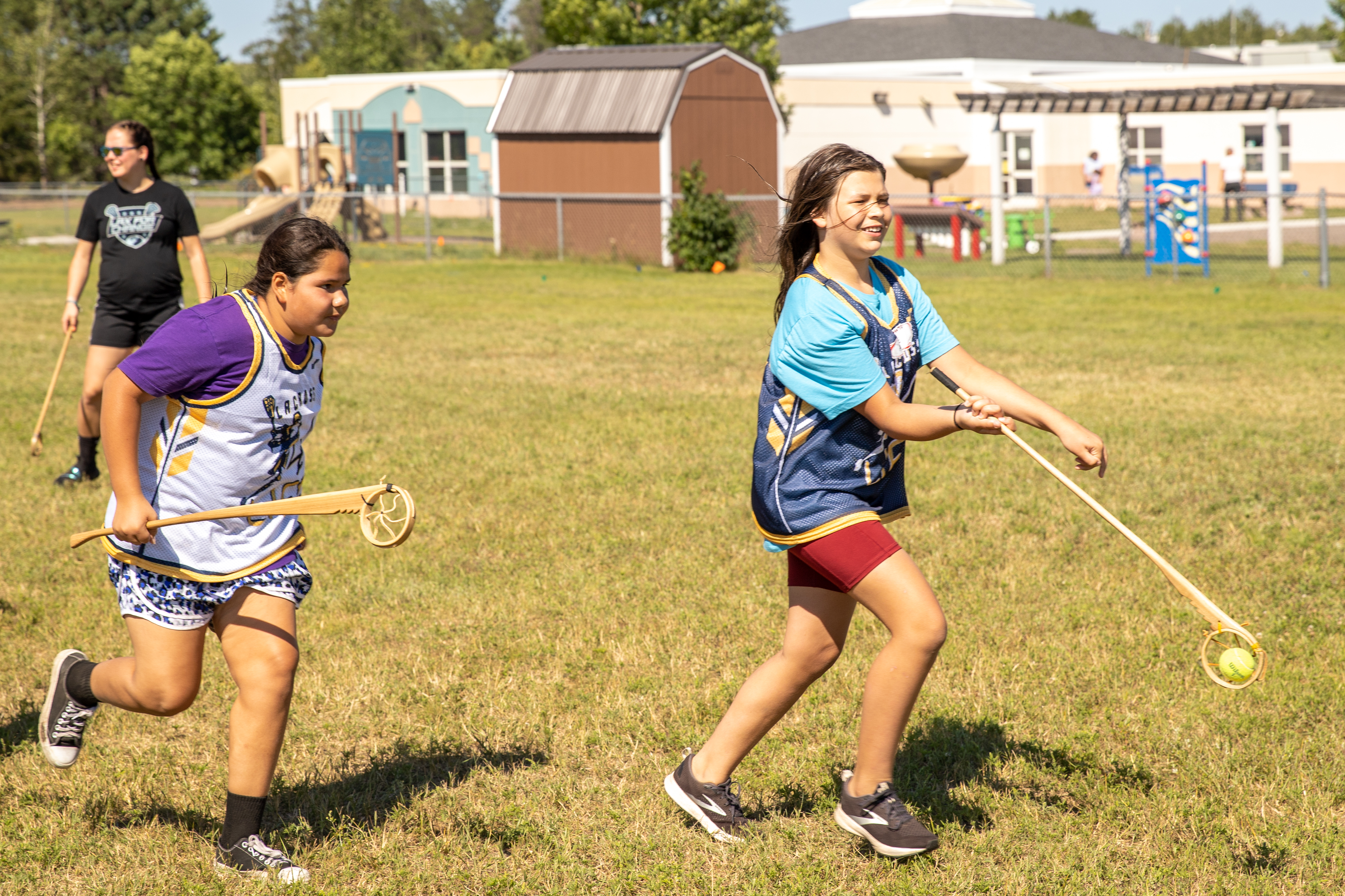 Two girls playing lacrosse in a field.