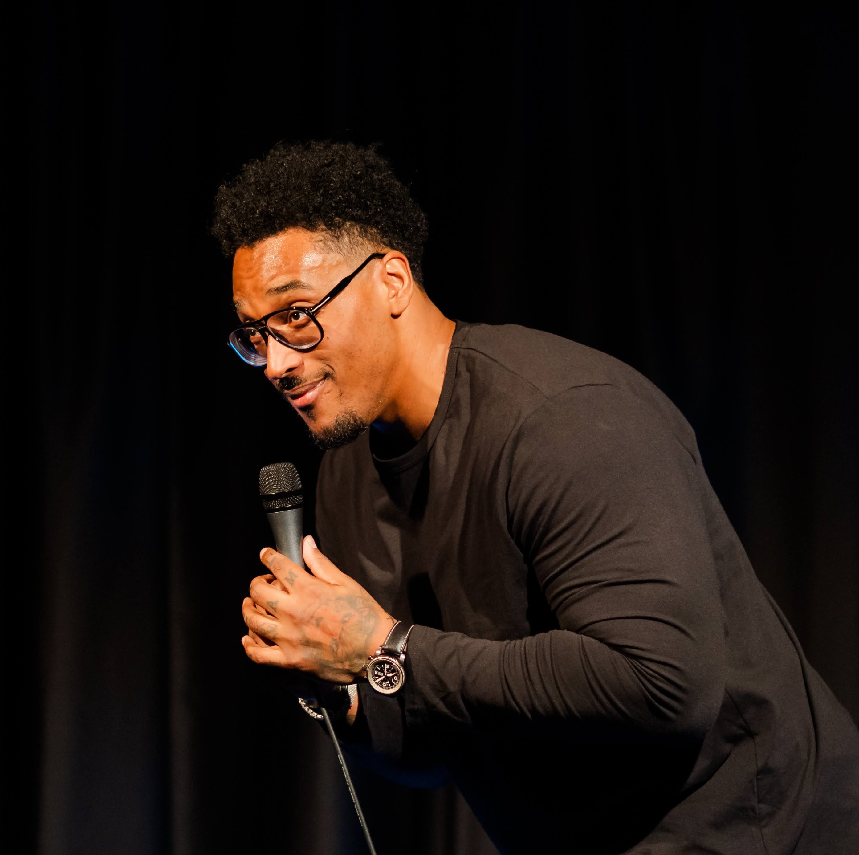 Joe Barksdale holding a microphone in both hands, leaning slightly forwards.